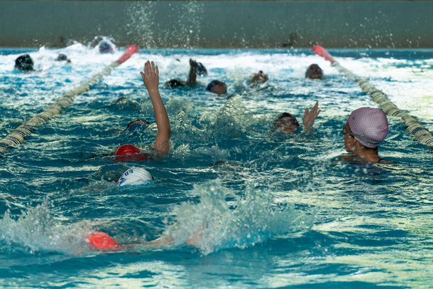 Dzieci pływające w wolnym stylu. Kryty basen z przejrzystą, błękitną wodą - Zdjęcie, obraz