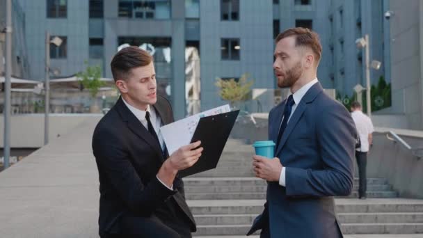 Two businessmen meeting discussing business on the background of the business district. Couple of businessmen having corporate break outside office building. Top managers are discussing the deal. - Footage, Video