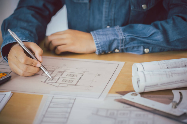Architekt nebo inženýr držící pero ukazující na stavební projektové vybavení na stole s plánem v kanceláři. - Fotografie, Obrázek
