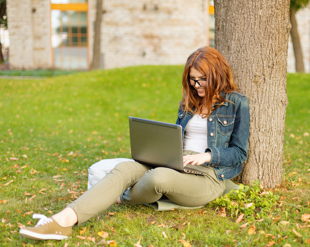 Smiling teenager in eyeglasses with laptop - Фото, изображение