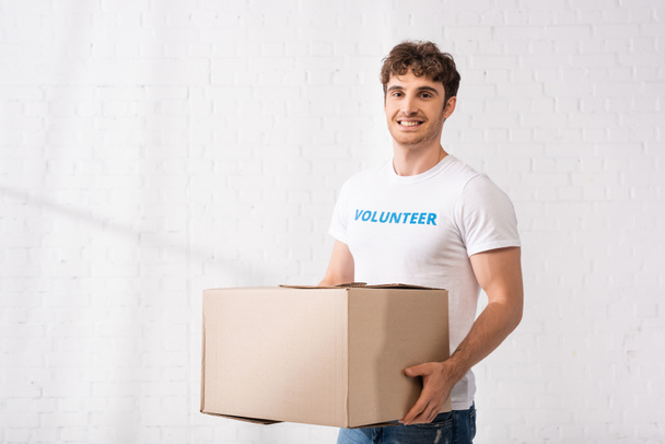 Volunteer looking at camera while holding package in charity center  - Photo, Image