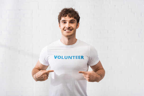 Giovane uomo che punta con le dita a lettering volontario su t-shirt  - Foto, immagini