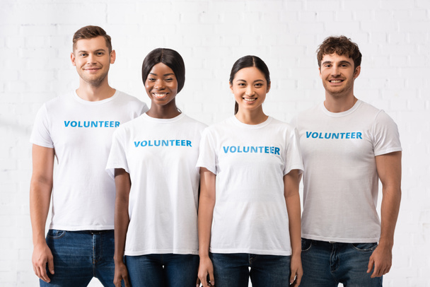 Молоді багатоетнічні люди з волонтерським написом на футболках, які дивляться на камеру
  - Фото, зображення