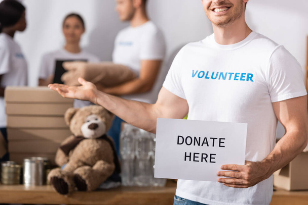 Focus selettivo del volontario in possesso di carta con donare oggi lettering e puntando con mano nel centro di beneficenza  - Foto, immagini
