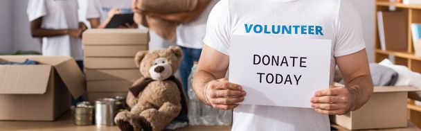 Foto panoramica di volontariato in possesso di carta con donare oggi lettering nel centro di beneficenza  - Foto, immagini