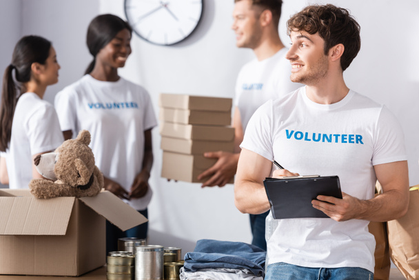 Selectieve focus van vrijwilligerswerk schrijven op klembord in de buurt van kleding en blikken in liefdadigheidscentrum  - Foto, afbeelding