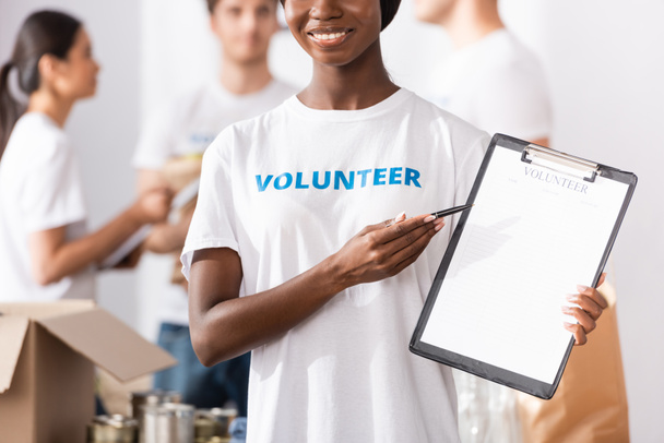 Enfoque selectivo del voluntario afroamericano apuntando al portapapeles en el centro de caridad  - Foto, Imagen