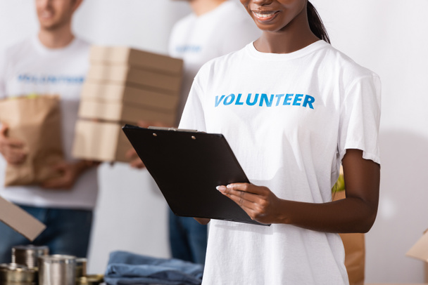 Cropped view of african american woman in t-shirt with volunteer lettering writing on clipboard  - Фото, изображение