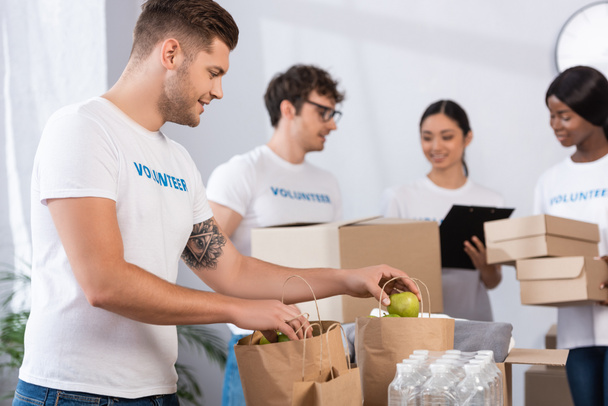 Concentration sélective d'un bénévole tenant des pommes près de sacs en papier dans un centre de bienfaisance  - Photo, image