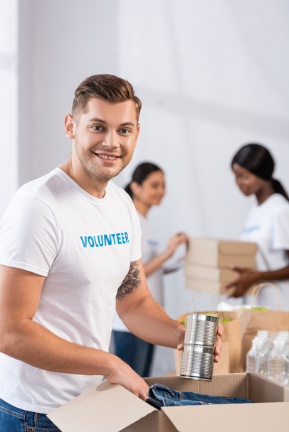 Selectieve focus van vrijwilliger die blikken in de buurt van pakket in liefdadigheidscentrum  - Foto, afbeelding