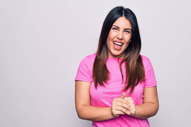 Young beautiful brunette woman wearing casual pink t-shirt standing over white background with hands together and crossed fingers smiling relaxed and cheerful. Success and optimistic - Photo, Image