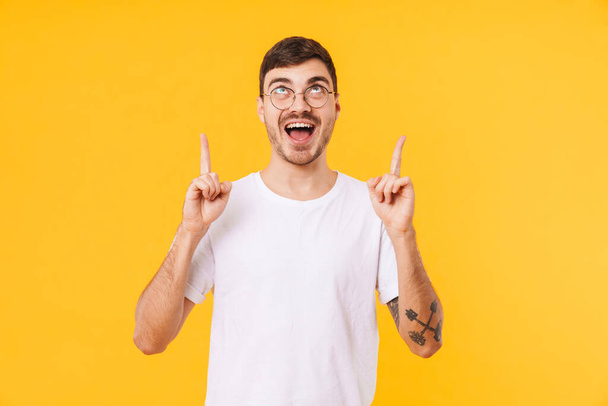 Photo of excited young man in eyeglasses pointing fingers upward isolated over yellow background - Фото, зображення