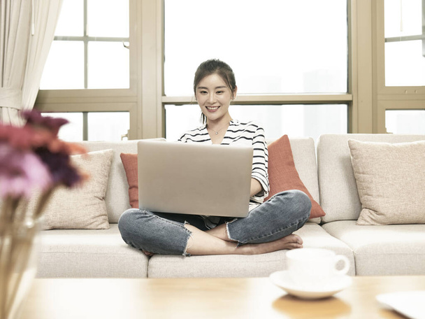 mladá asijská podnikatelka pracující z domova sedí na gauči pomocí notebooku - Fotografie, Obrázek