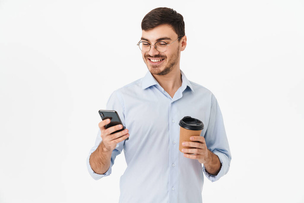 Gözlüklü, kahve içen ve beyaz arka planda izole edilmiş cep telefonu kullanan mutlu beyaz adamın fotoğrafı. - Fotoğraf, Görsel