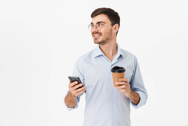 Photo of happy caucasian man in eyeglasses drinking coffee and using cellphone isolated over white background - Foto, imagen