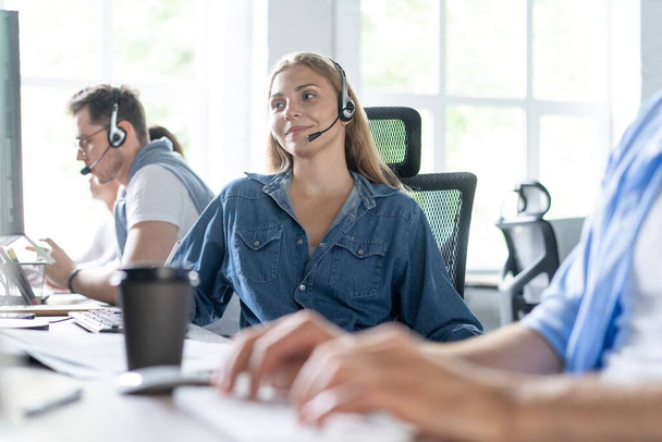 ¿Cómo puedo ayudarle Hermosos trabajadores del centro de llamadas en los auriculares están trabajando en la oficina moderna - Foto, imagen