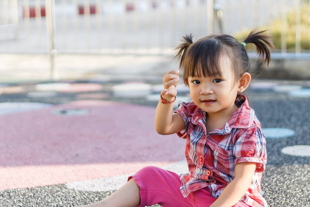 Портретний образ дитини віком 2 роки. Щаслива азіатська дівчинка сидить на гнучкому поверсі біля ігрового майданчика. Вона посміхається і штовхає правою рукою вгору. - Фото, зображення
