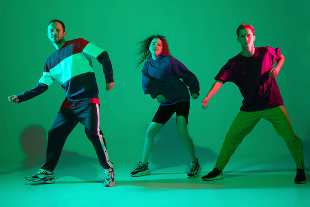 Stylish men and woman dancing hip-hop in bright clothes on gradient background at dance hall in neon light - Foto, Imagem