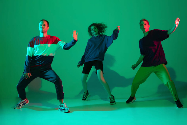 Stylish men and woman dancing hip-hop in bright clothes on gradient background at dance hall in neon light - Valokuva, kuva