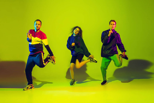 Stylish men and woman dancing hip-hop in bright clothes on gradient background at dance hall in neon light - Fotó, kép