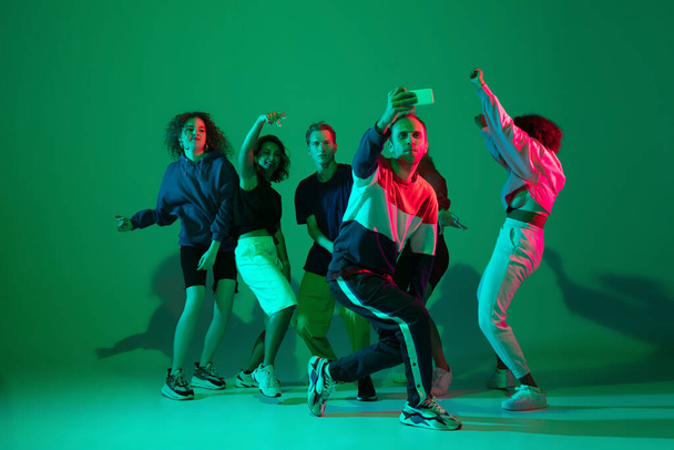 Stylish men and woman dancing hip-hop in bright clothes on gradient background at dance hall in neon light - Fotoğraf, Görsel
