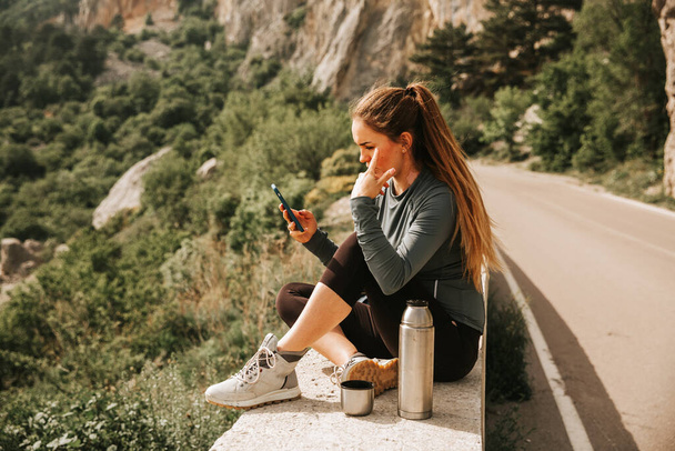 Traveling woman sitting near mountain and looking far away Spring weather, calm scene. Hiking outdoors, landscape view in the sunlight. A series of photos of Wanderlust. - Photo, Image