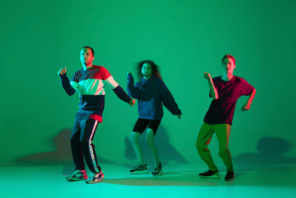 Stylish men and woman dancing hip-hop in bright clothes on gradient background at dance hall in neon light - Foto, Imagen