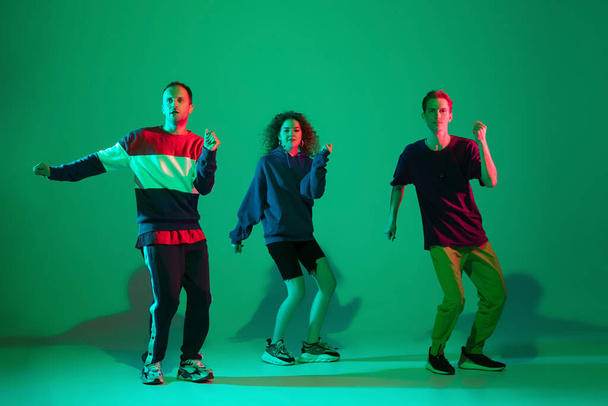 Stylish men and woman dancing hip-hop in bright clothes on gradient background at dance hall in neon light - Φωτογραφία, εικόνα