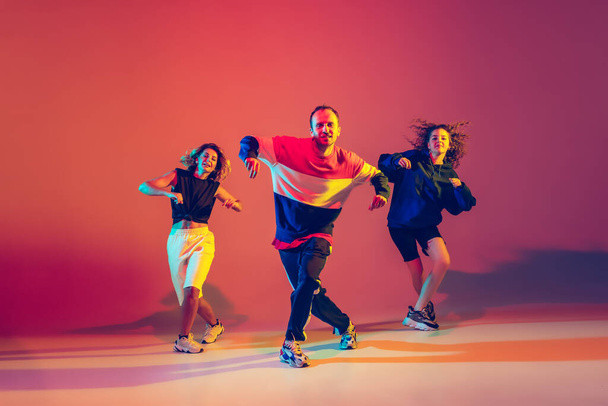 Stylish man and women dancing hip-hop in bright clothes on gradient background at dance hall in neon light - Fotografie, Obrázek