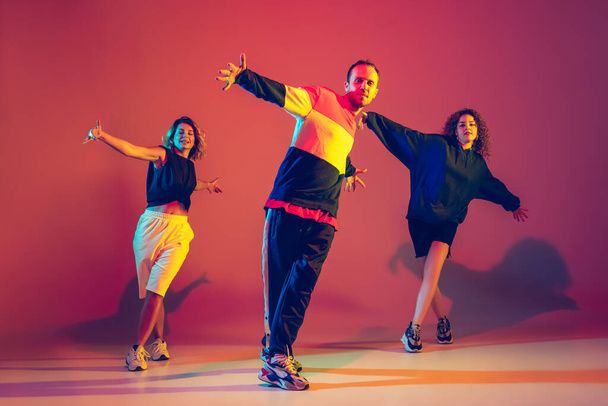 Stylish man and women dancing hip-hop in bright clothes on gradient background at dance hall in neon light - Foto, Bild