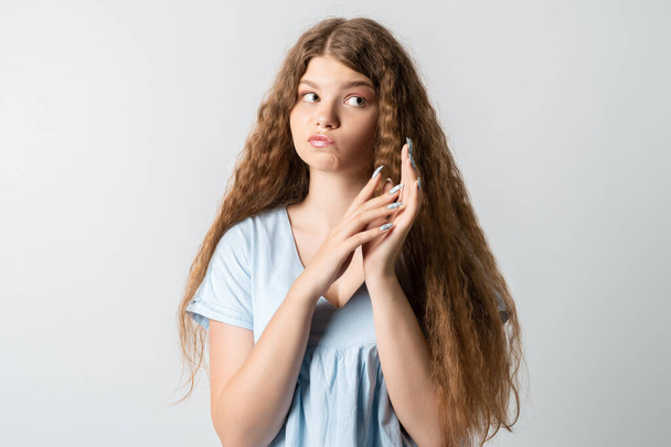 Zdjęcie zamyślonej europejskiej młodej kobiety z kręconymi długimi włosami, z wymarzonym wyrazem twarzy na bok. Izolacja na białym tle. - Zdjęcie, obraz