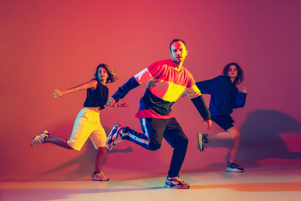 Stylish man and women dancing hip-hop in bright clothes on gradient background at dance hall in neon light - Fotó, kép