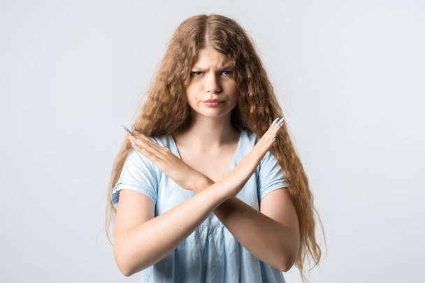 Emocionální evropská mladá žena s kudrnatými dlouhými vlasy oblečená v neformálním oblečení, ukazuje gesto STOP na bílém pozadí. Nedovolte násilí, zastavte válku, milujte. - Fotografie, Obrázek