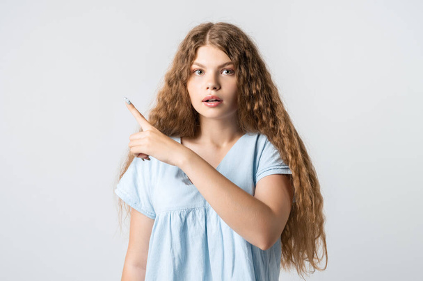 Jobb, ha megnézed. Kíváncsivá tett európai lány göndör hosszú hajjal, egy ujjal mutogatva, üres teret mutat az előléptetésednek. Emberek, reklám koncepció - Fotó, kép