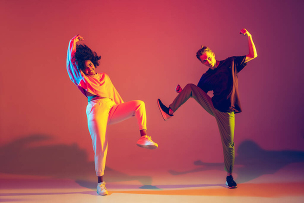 Stylish man and woman dancing hip-hop in bright clothes on gradient background at dance hall in neon light - Valokuva, kuva