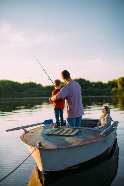 Young family fishing on boat in summertime. Father teaches son fishing. Back view. Photo for blog about family travel - Fotoğraf, Görsel