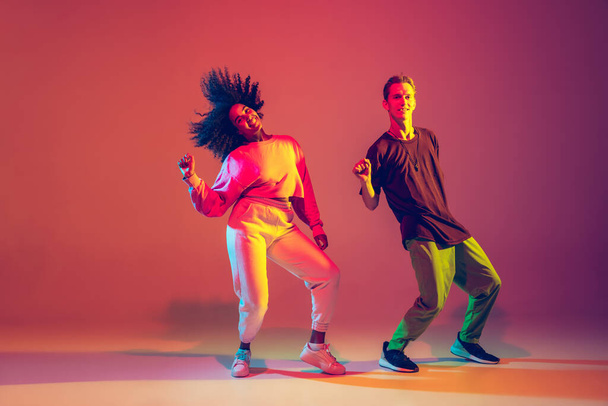 Stylish man and woman dancing hip-hop in bright clothes on gradient background at dance hall in neon light - Fotografie, Obrázek