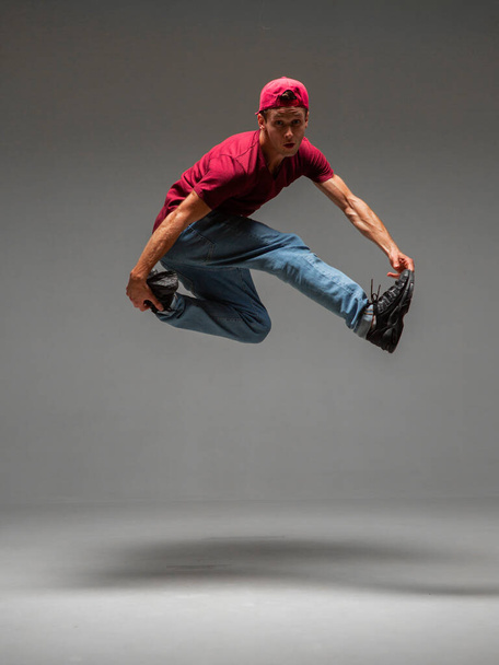 Cool young guy breakdancer jumps in studio on gray background. Battle competitions announcement - Foto, Imagem