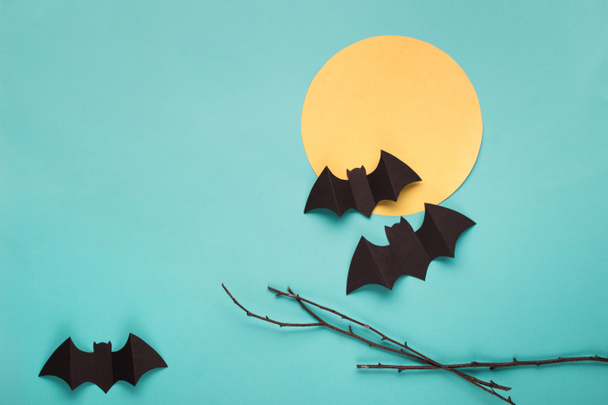 Halloween paper decorations on blue background. Black bats, tree branch and moon. Halloween concept. Flat lay, top view, overhead. Minimal style. Halloween party greeting card mockup with copy space.  - Foto, immagini