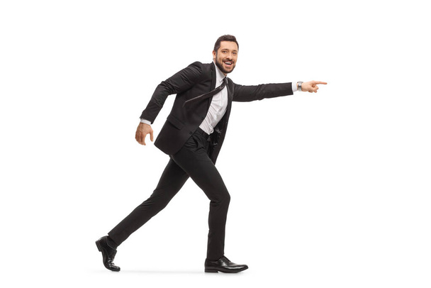 Schöner Mann im schwarzen Anzug läuft und zeigt vereinzelt auf weißen Hintergrund - Foto, Bild