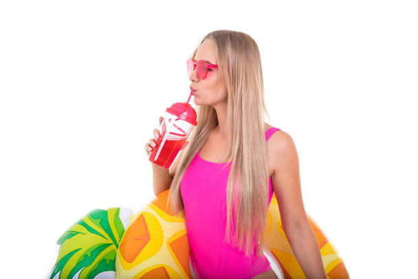 Pembe mayo giymiş bir kız şişme yüzme çemberi tutuyor ve limonata içiyor. - Fotoğraf, Görsel