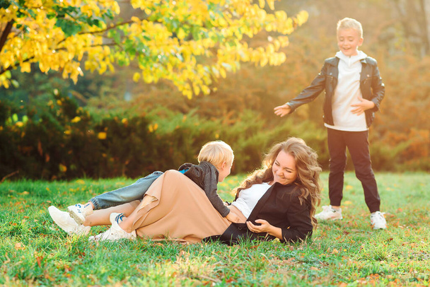 Η μητέρα και τα παιδιά διασκεδάζουν έξω. Μοντέρνο οικογενειακό περπάτημα στην φθινοπωρινή φύση. Οικογένεια, μόδα και τρόπος ζωής. Μητέρα με παιδιά που περπατάει στο πάρκο το φθινόπωρο. Διακοπές το φθινόπωρο. - Φωτογραφία, εικόνα