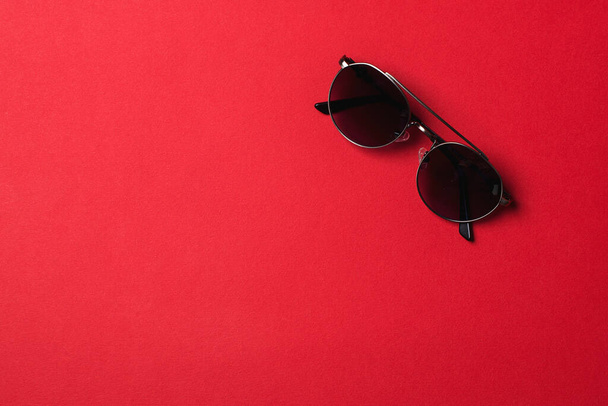 Kırmızı arka planda izole edilmiş moda güneş gözlükleri. Yaz modası, alışveriş ve satış. Siyah güneş gözlüğü. Uzayı kopyala Koruma gözleri için modern aksesuar. - Fotoğraf, Görsel