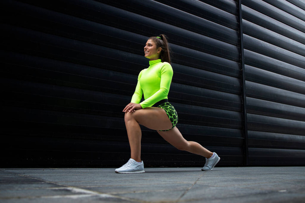 Aufnahme einer muskulösen sexy Sportlerin mit langen Haaren und kräftigen Beinen, die sich im Fitnessstudio vor schwarzem Hintergrund dehnt und aufwärmt. Fitness und Bodybuilding. - Foto, Bild