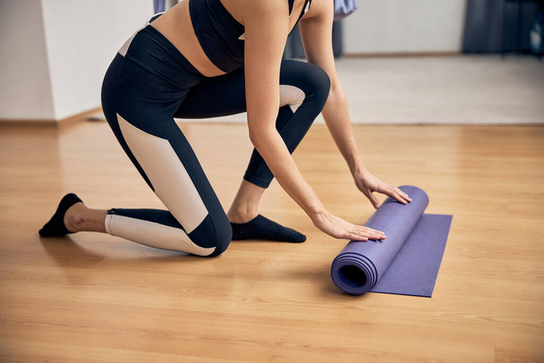 Mani di sporty giovane donna pieghevole tappetino yoga - Foto, immagini