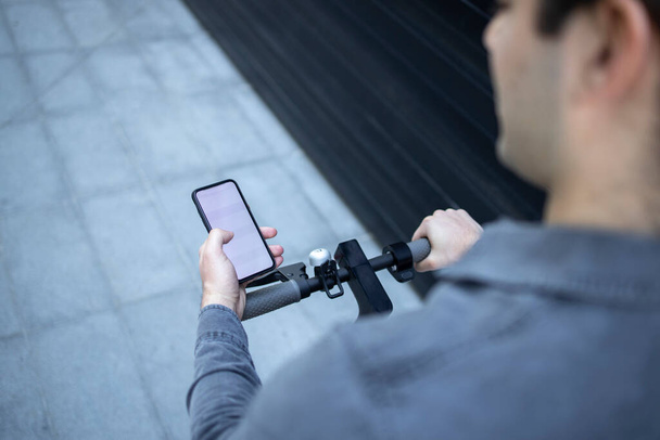 Nagy látószögű kilátás felismerhetetlen üzletember használja app az ő okos telefon lovaglás közben elektromos robogó. - Fotó, kép
