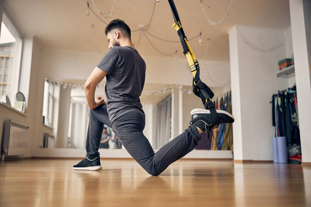 Sporty male doing a TRX lunge exercise - Photo, Image