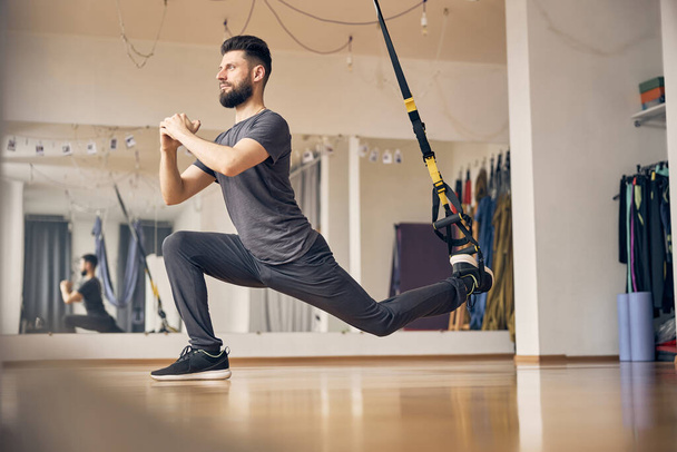 Dreamy young athlete performing a TRX lunge - Foto, afbeelding