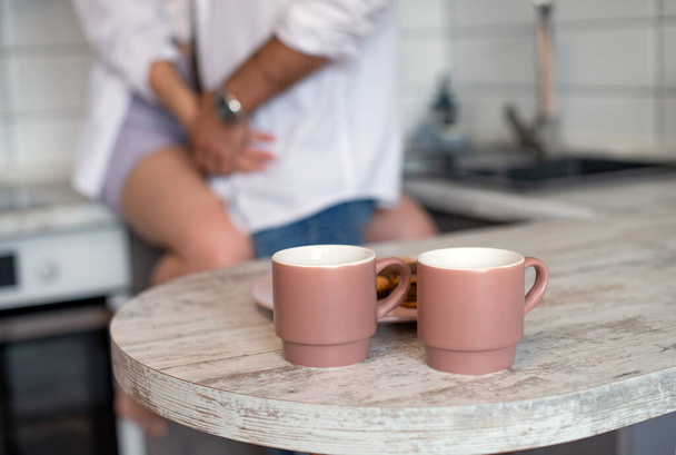 Un par de tazas de café rosado. Cocinas en colores claros. Rutina de la mañana, preparación del desayuno. Interior moderno en el estilo del minimalismo. Té caliente con galletas. Suave mañana para una pareja enamorada cogida de la mano - Foto, Imagen