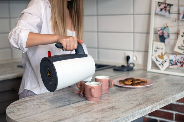A pair of pink coffee cups. Kitchens in light colors. Morning routine, breakfast preparation. Modern interior in the style of minimalism. Hot tea with cookies. Girl pours from a teapot - Φωτογραφία, εικόνα